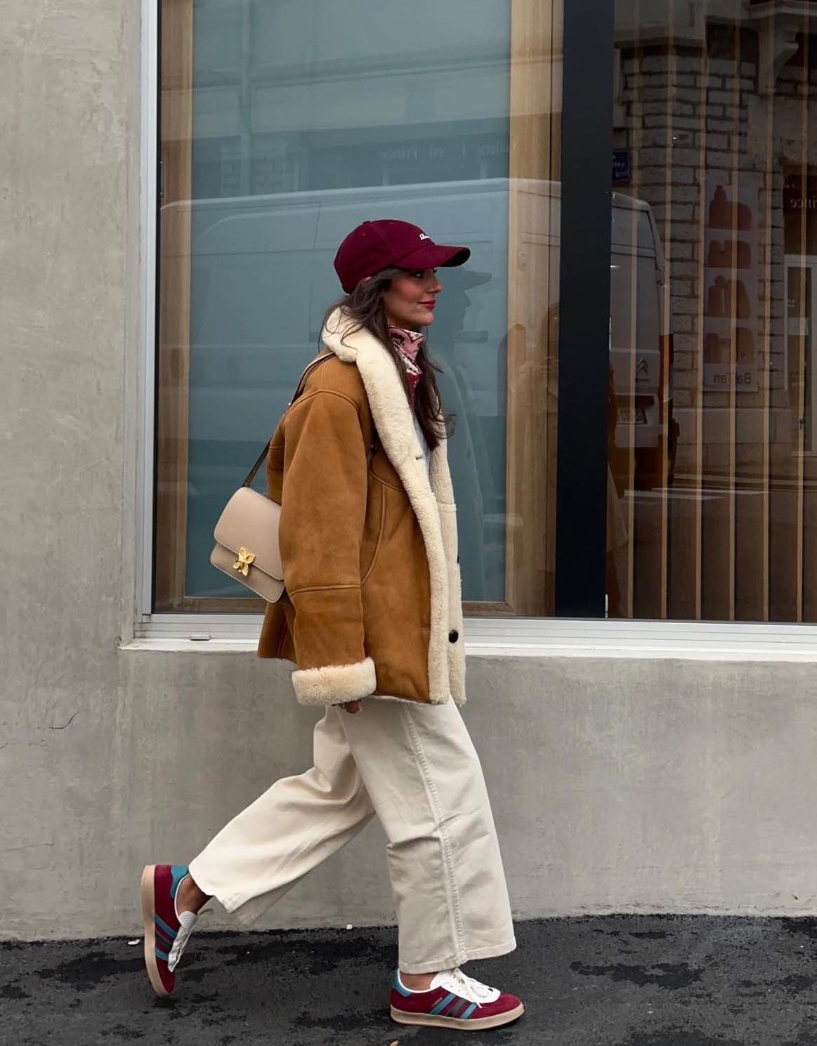 Baggy white jeans with a brown shearing jacket, burgundy Adidas sneakers and a burgundy cap.