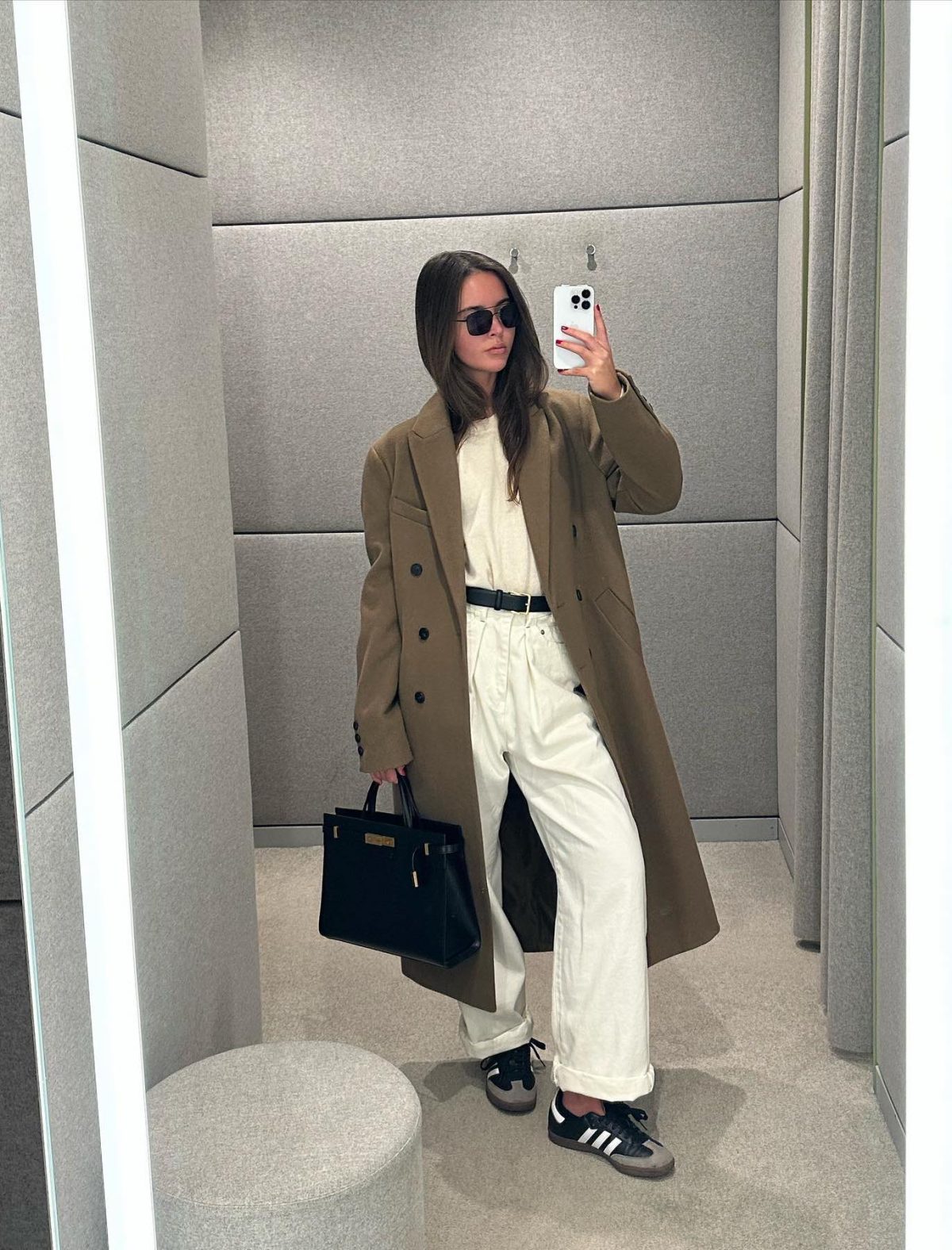Baggy white jeans with a khaki green trench coat, black Adidas Samba sneakers and black YSL Manhattan bag.